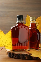 Photo of Bottles of tasty maple syrup and dry leaves on wooden table