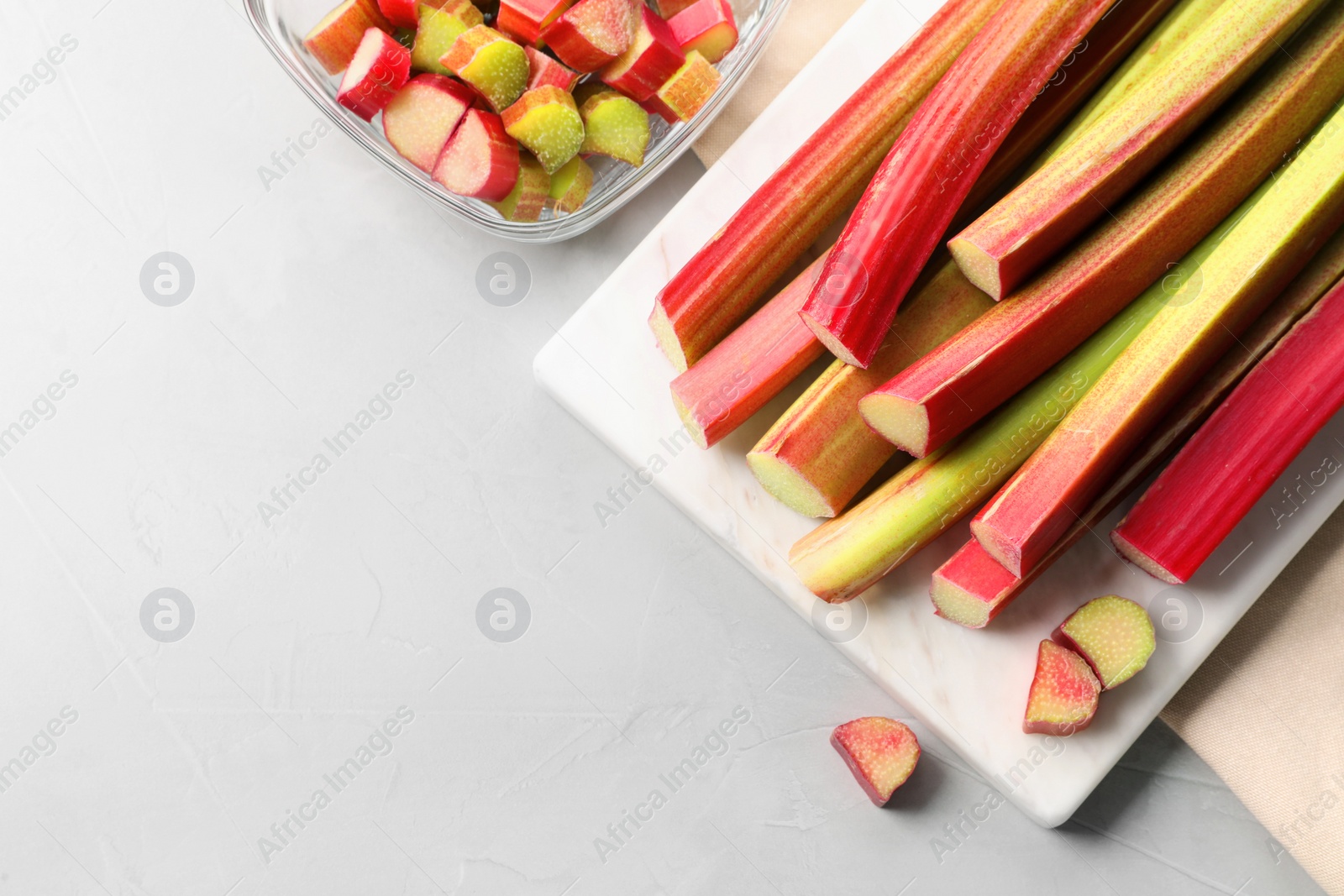 Photo of Whole and cut rhubarb stalks on white table, flat lay. Space for text