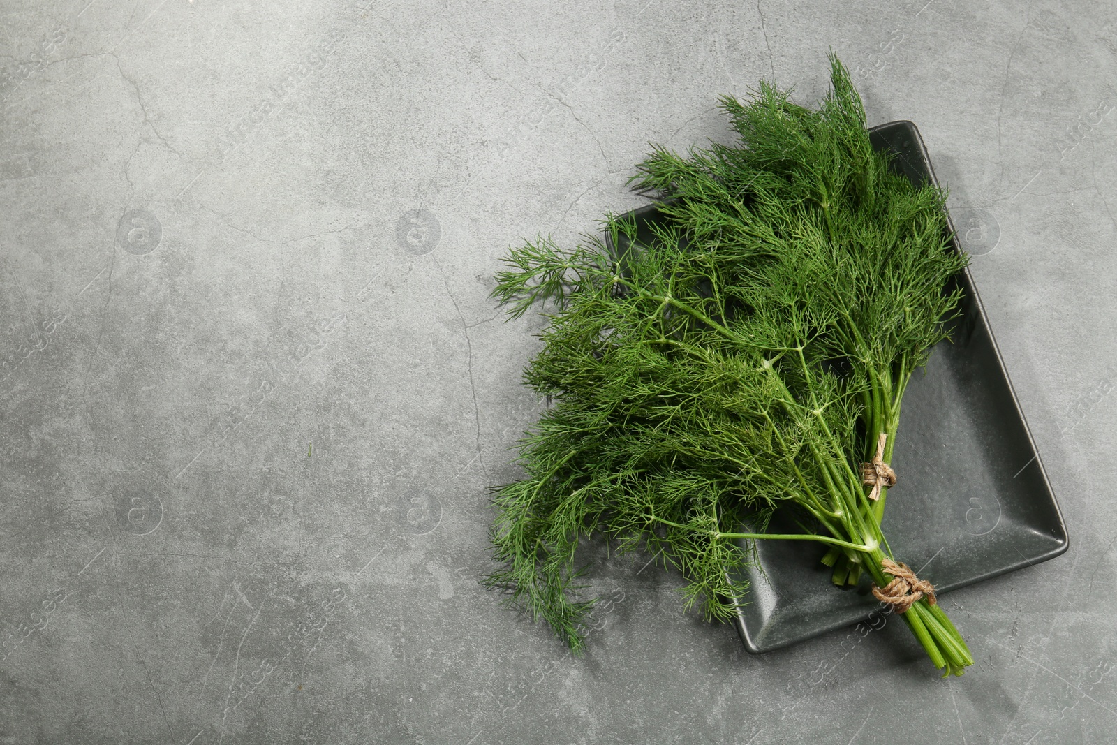 Photo of Plate with bunch of fresh green dill on light grey table, top view. Space for text