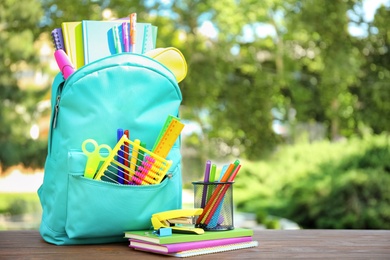 Photo of Bright backpack and school stationery on table outdoors, space for text