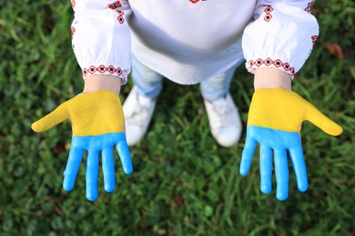 Little girl with hands painted in Ukrainian flag colors outdoors, top view. Love Ukraine concept