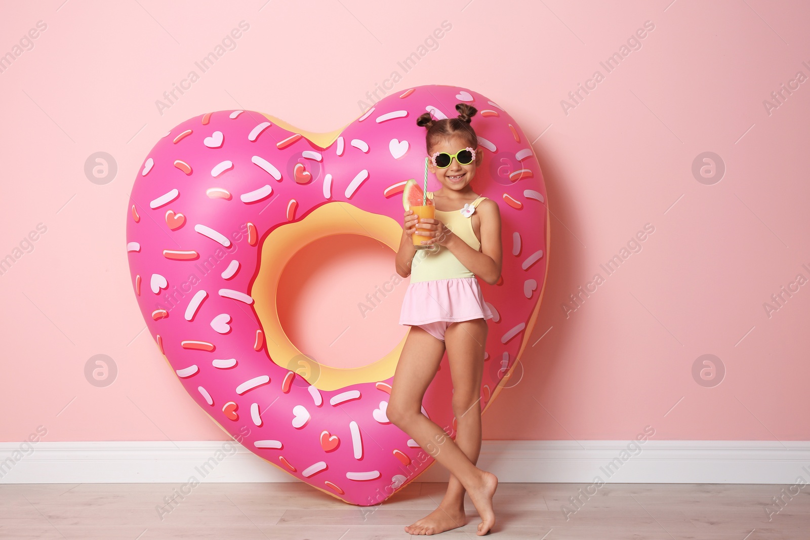 Photo of Cute little girl with inflatable heart and glass of cocktail near color wall