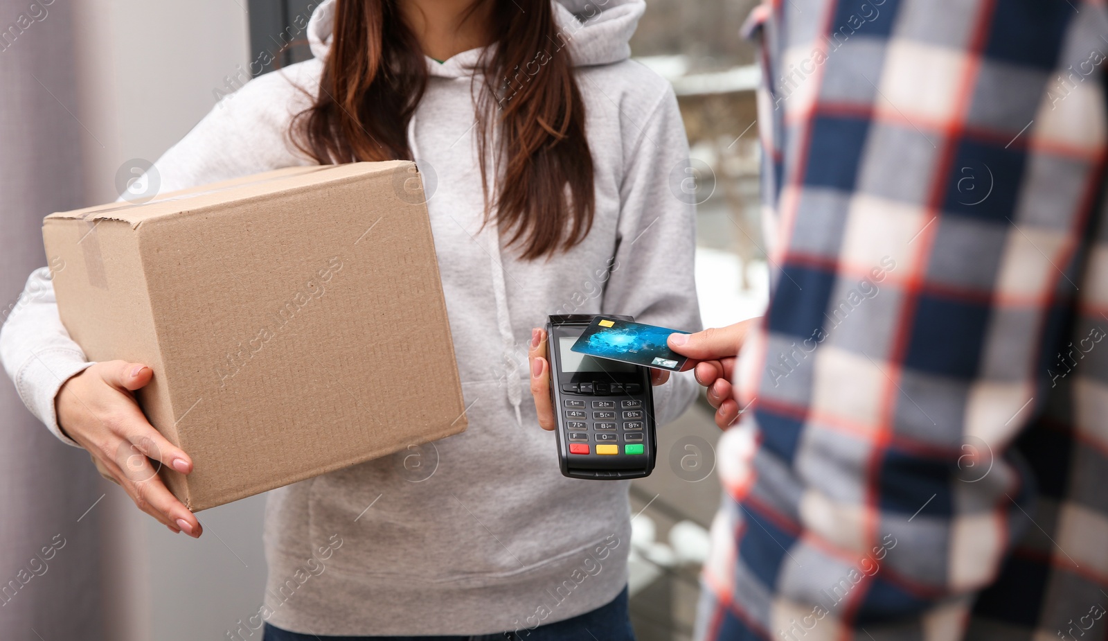 Photo of Young man with credit card using bank terminal for delivery payment at doorway, closeup