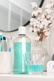 Photo of Bottle of mouthwash and glass on white table in bathroom