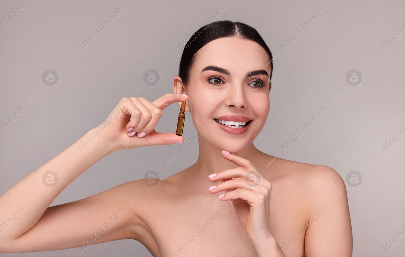 Photo of Beautiful young woman holding skincare ampoule on grey background