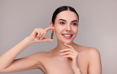 Beautiful young woman holding skincare ampoule on grey background