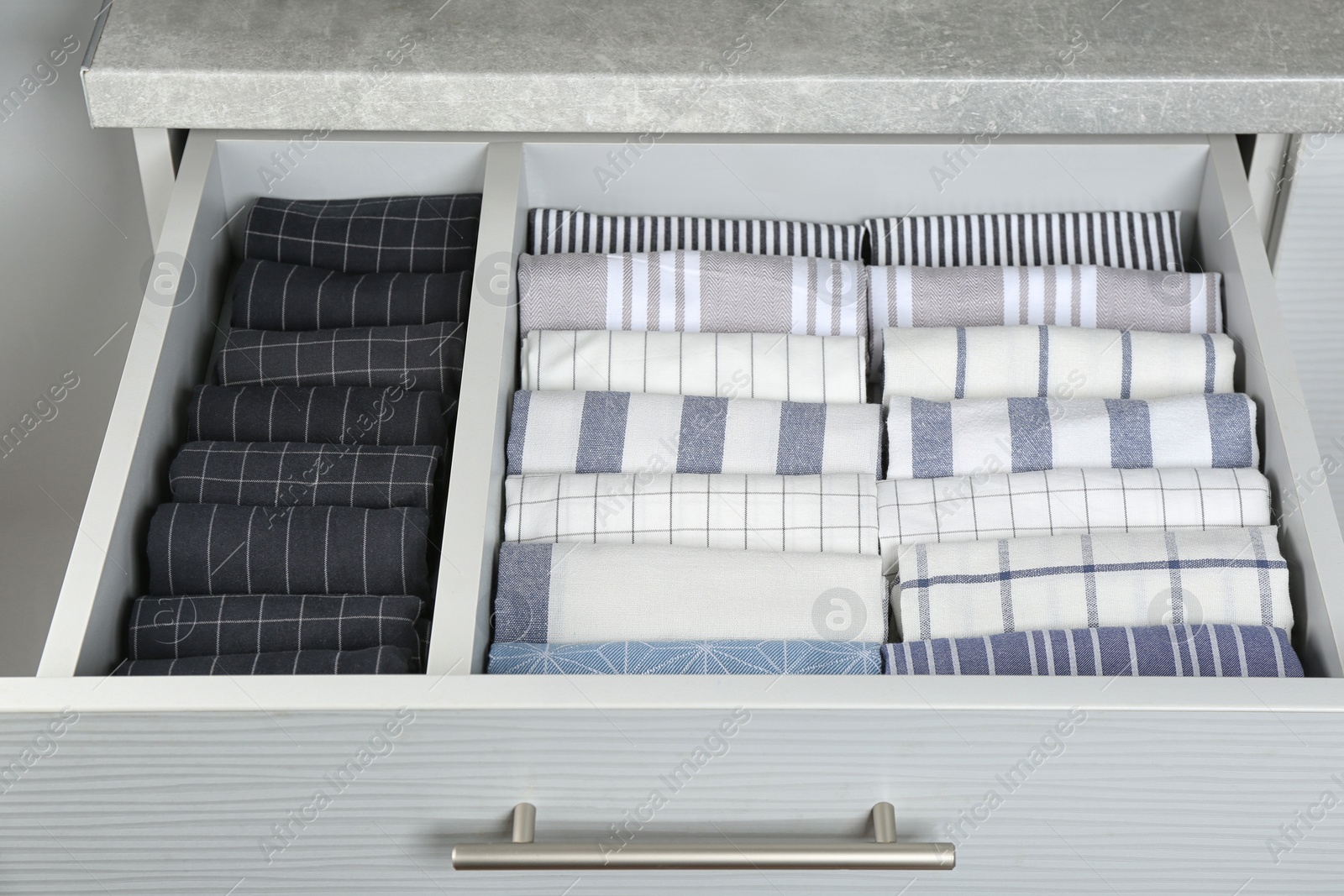 Photo of Open drawer with folded towels, closeup. Order in kitchen