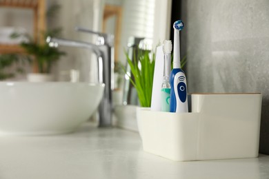 Photo of Electric toothbrushes and tube of paste on white countertop in bathroom. Space for text