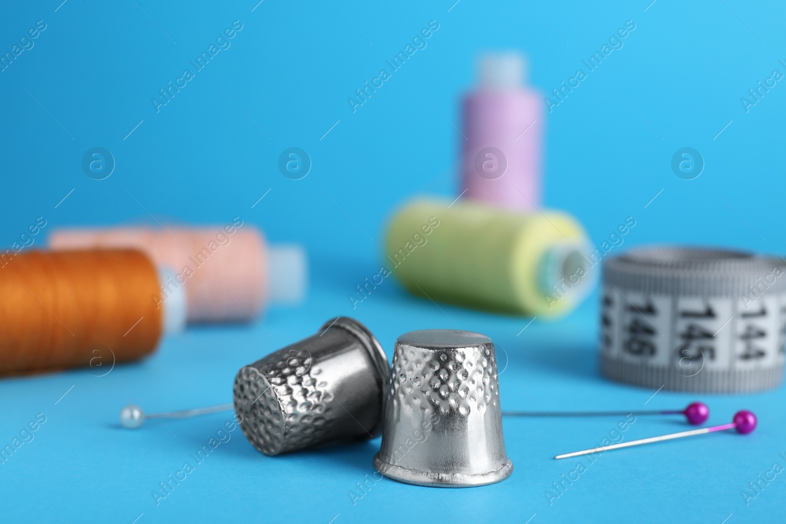 Photo of Silver thimbles on light blue background. Sewing accessories