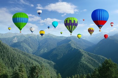 Image of Bright hot air balloons flying in sky with clouds over mountains