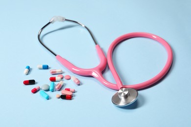 Stethoscope and pills on light blue background, closeup. Medical tool