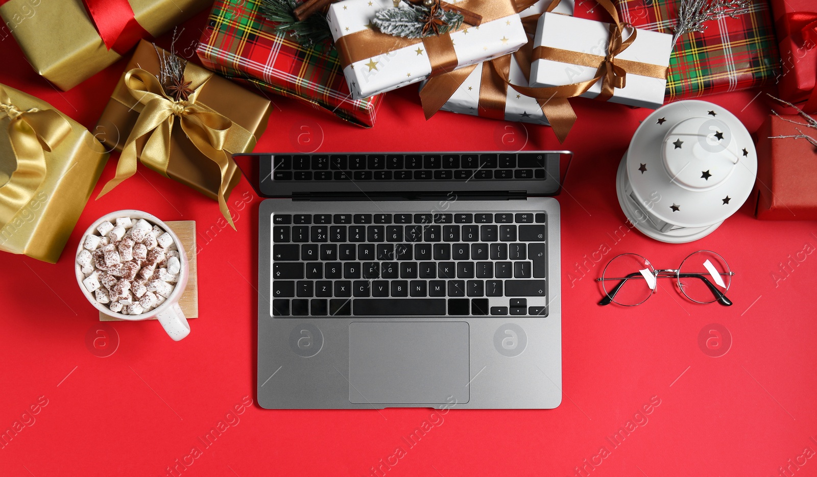 Photo of Flat lay composition with laptop, gift boxes, eyeglasses and cup of drink on red background. Letter for Santa