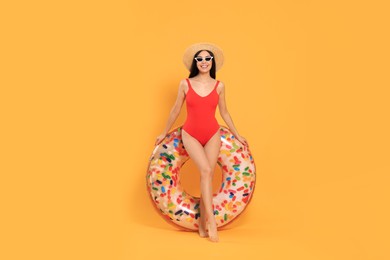 Photo of Happy young woman with beautiful suntan, hat, sunglasses and inflatable ring against orange background