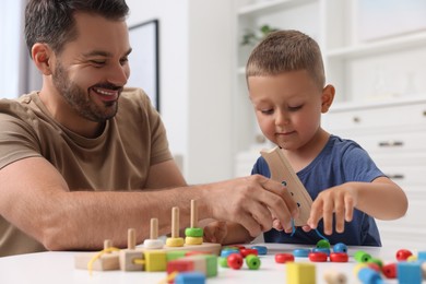 Photo of Motor skills development. Father and his little son playing with wooden lacing toy at white table indoors