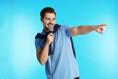 Photo of Young handsome man in casual clothes singing with microphone on color background