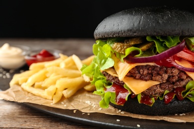 Photo of Plate with black burger and French fries on table, closeup. Space for text