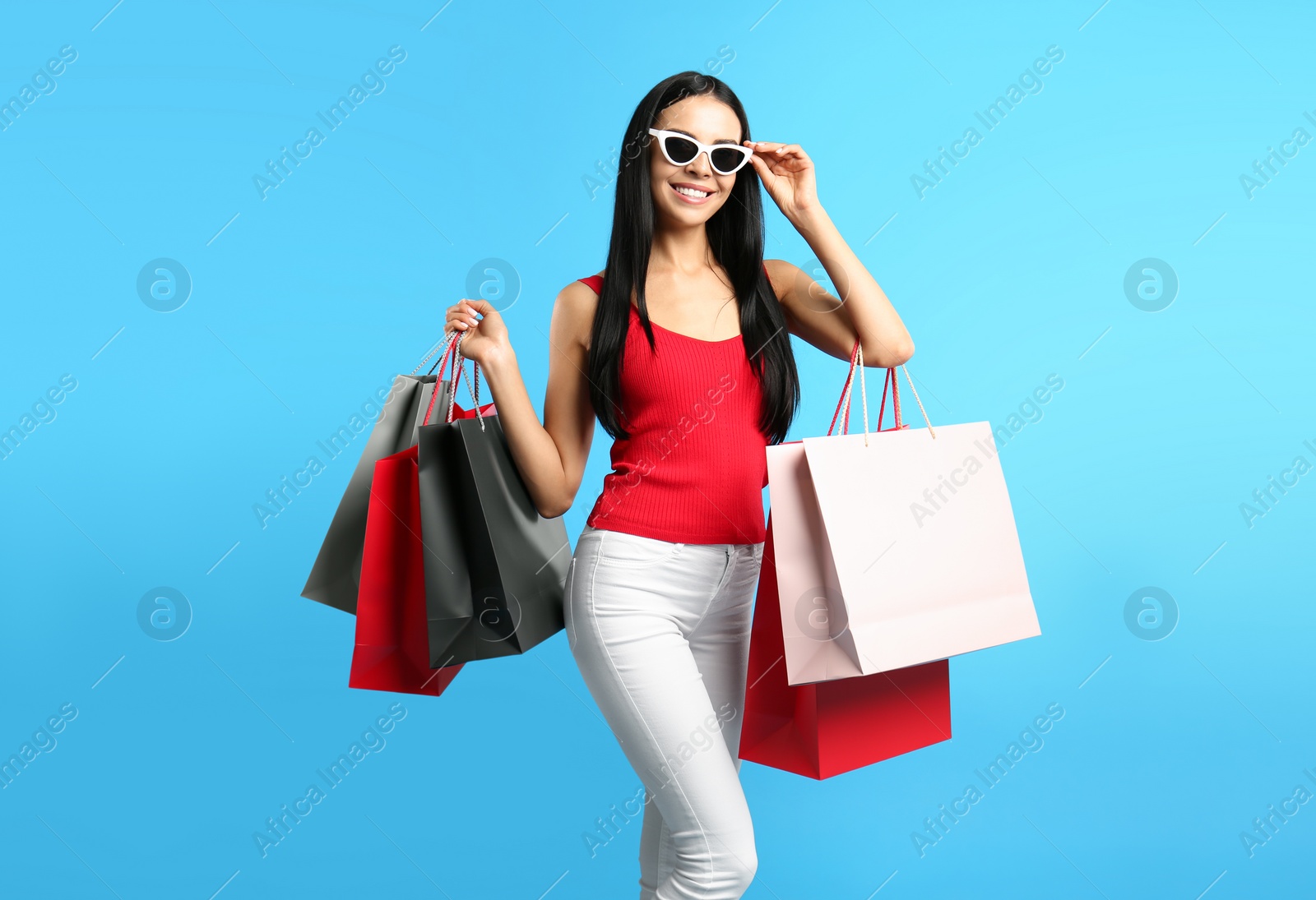 Photo of Beautiful young woman with paper shopping bags on light blue background