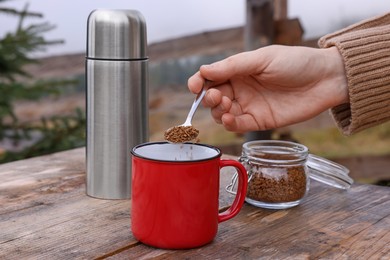 Photo of Woman making instant coffee at wooden table outdoors, closeup