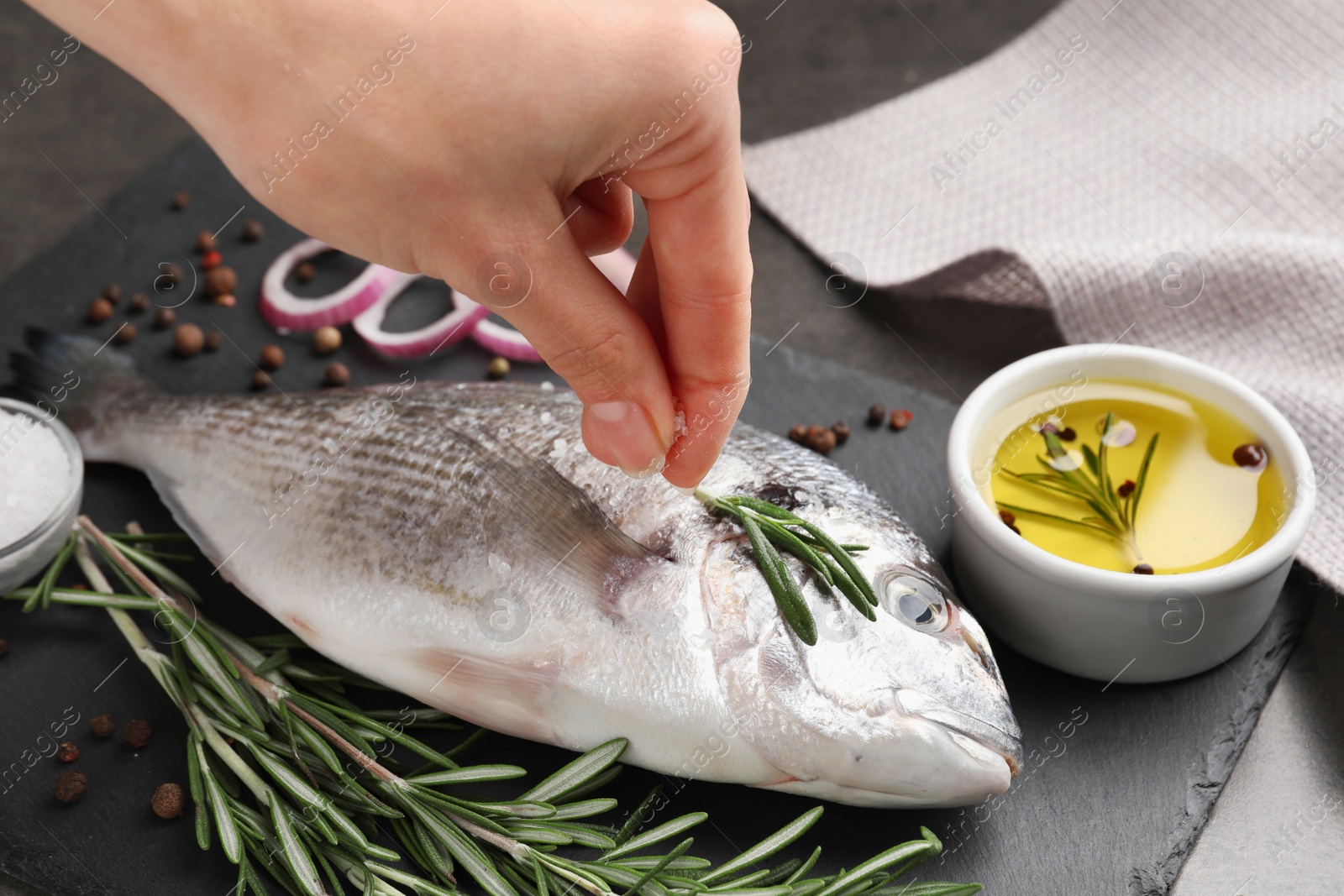 Photo of Woman salting fresh dorado fish on black slate board, closeup