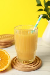 Glass of fresh orange juice and stylish coaster on white wooden table