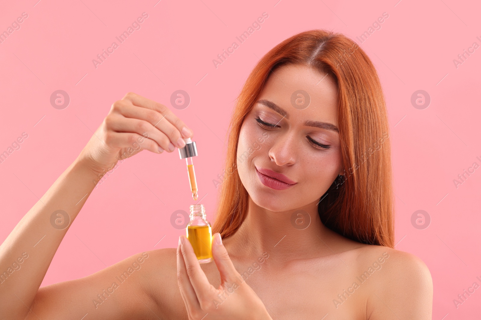 Photo of Beautiful young woman with bottle of cosmetic serum on pink background