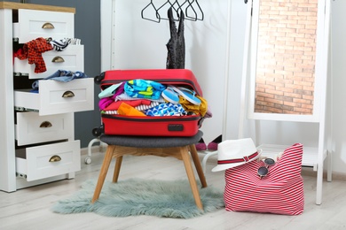 Photo of Suitcase with beach clothes and accessories on stool in dressing room