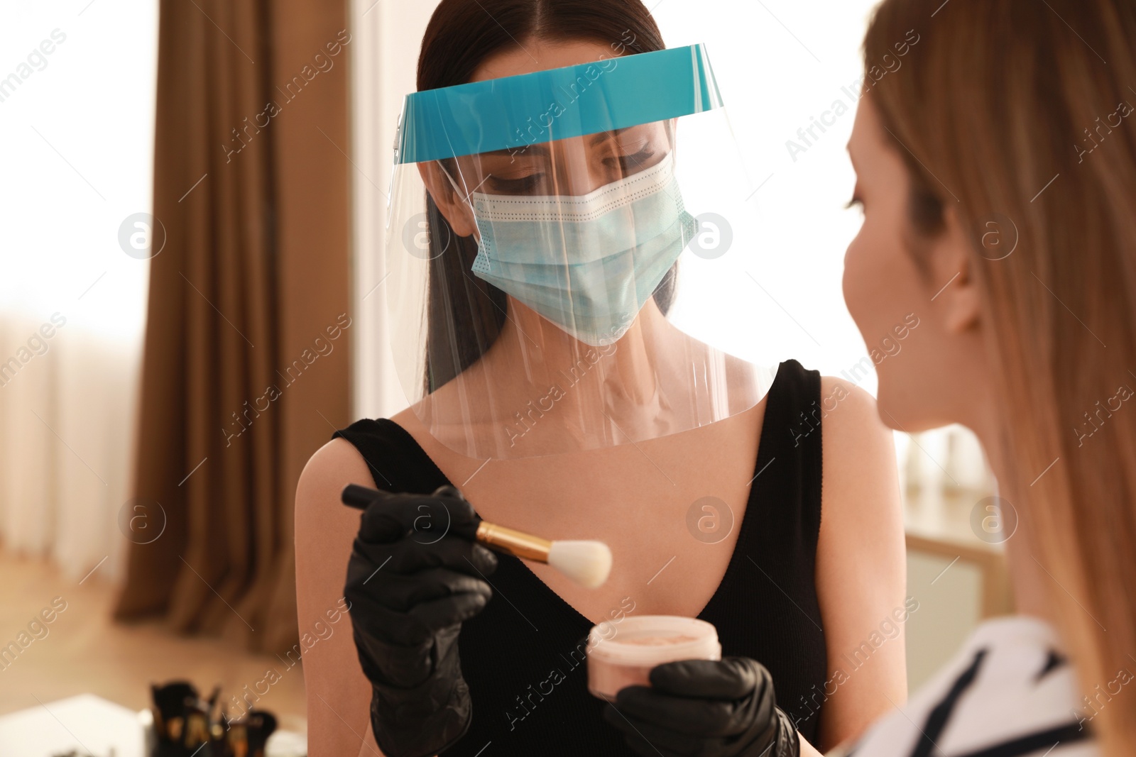 Photo of Makeup artist in protective mask and gloves working with woman indoors. Preventive measures during COVID-19 pandemic