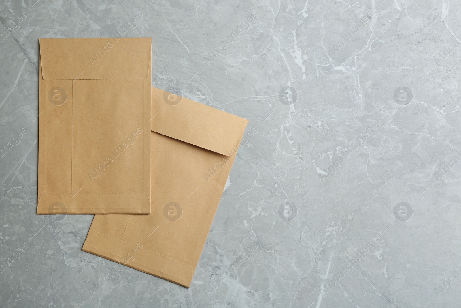 Photo of Kraft paper envelopes on grey marble background, flat lay. Space for text