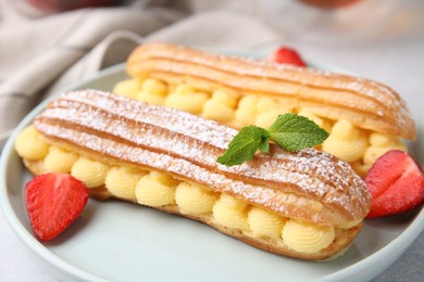 Delicious eclairs filled with cream, strawberries and mint on table, closeup