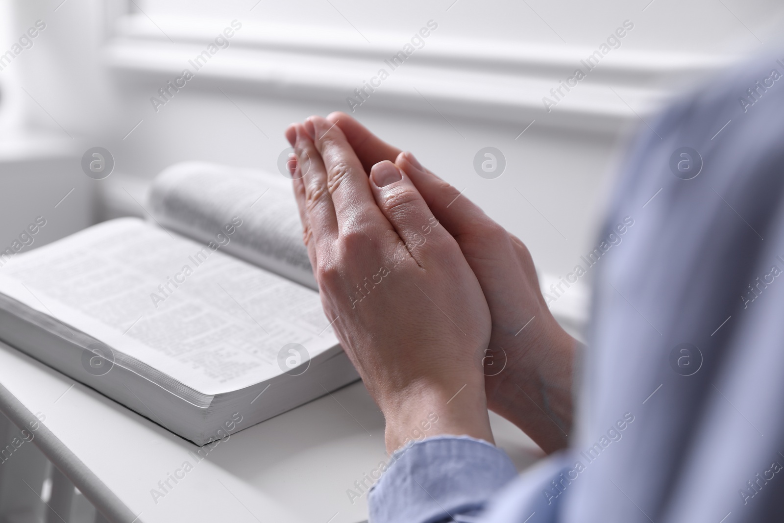 Photo of Religion. Christian woman praying over Bible indoors, closeup