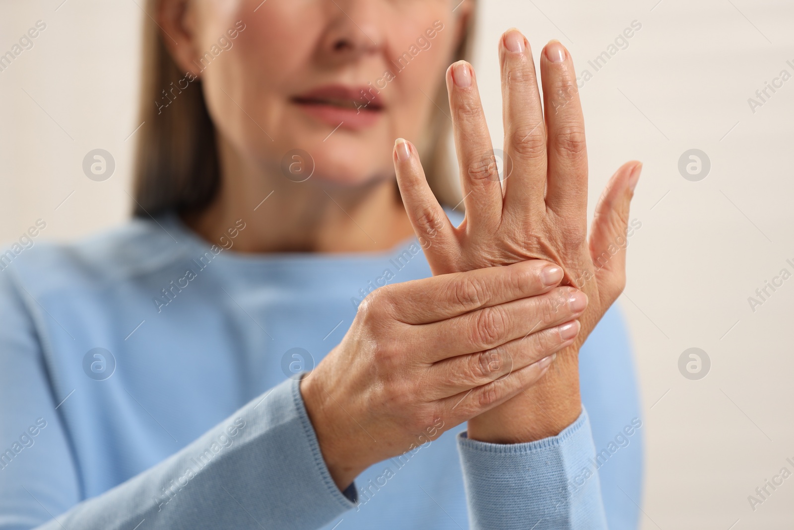 Photo of Mature woman suffering from pain in hand against light grey background, closeup. Rheumatism symptom
