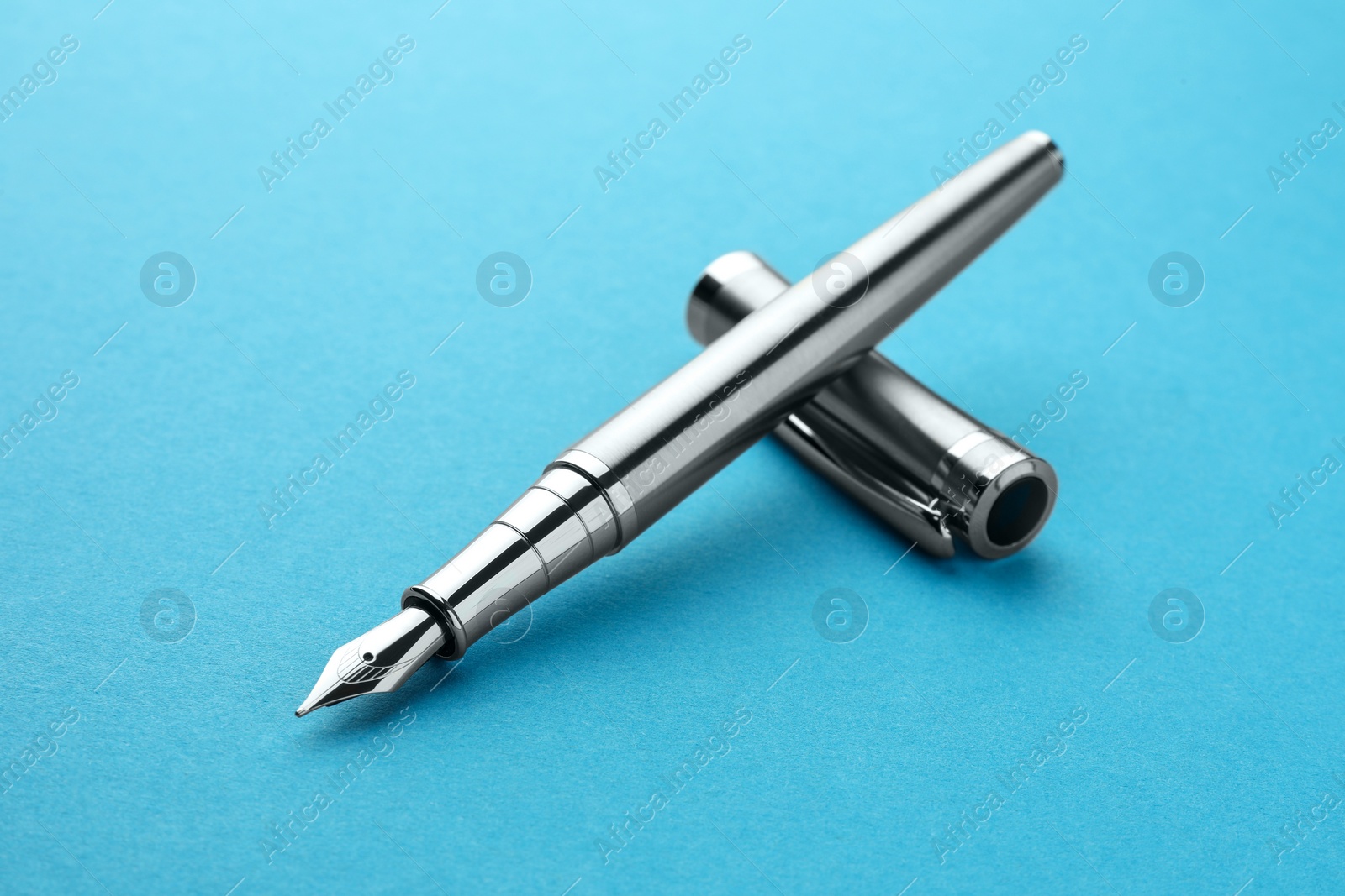 Photo of Stylish silver fountain pen with cap on light blue background, closeup
