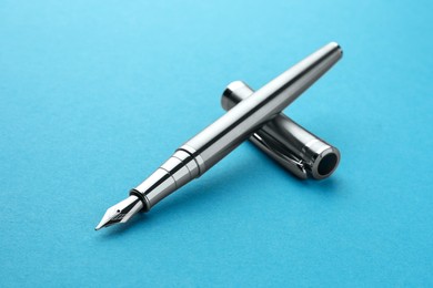 Photo of Stylish silver fountain pen with cap on light blue background, closeup