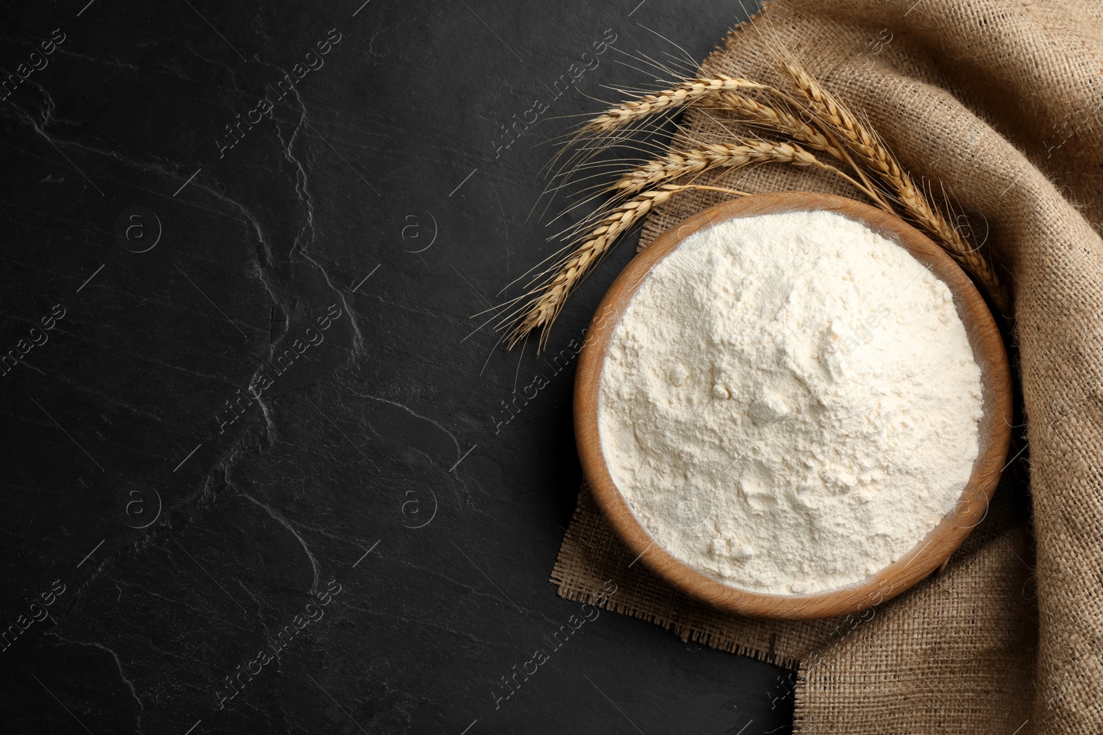 Photo of Flour, wheat ears and sackcloth on black table, flat lay. Space for text