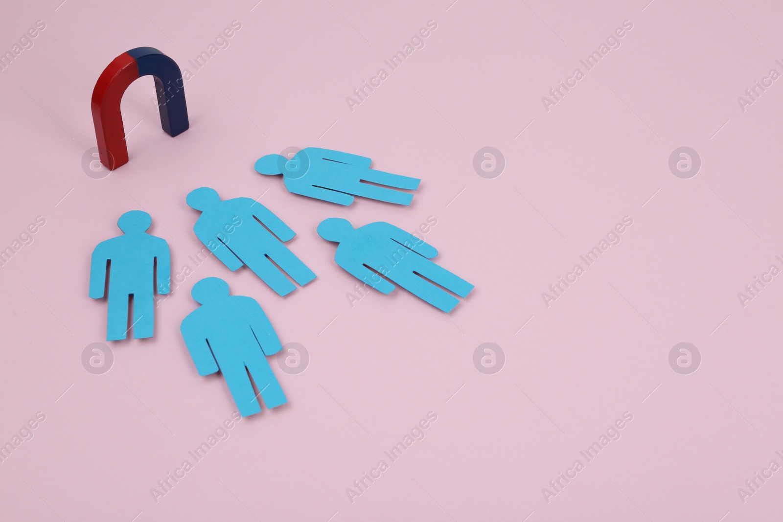 Photo of Magnet attracting paper people on pink background. Space for text