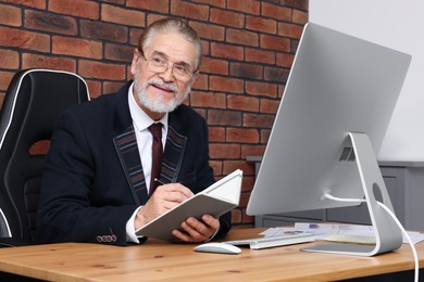 Photo of Happy senior boss working at wooden table in office