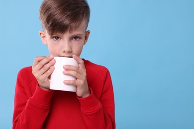 Photo of Cute boy drinking beverage from white ceramic mug on light blue background, space for text