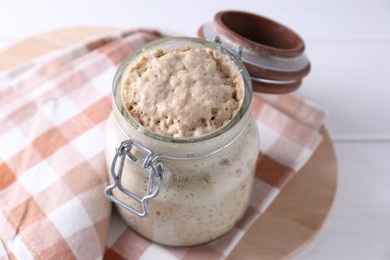 Photo of Sourdough starter in glass jar on white wooden table, closeup