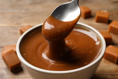 Taking yummy salted caramel with spoon from bowl at wooden table, closeup