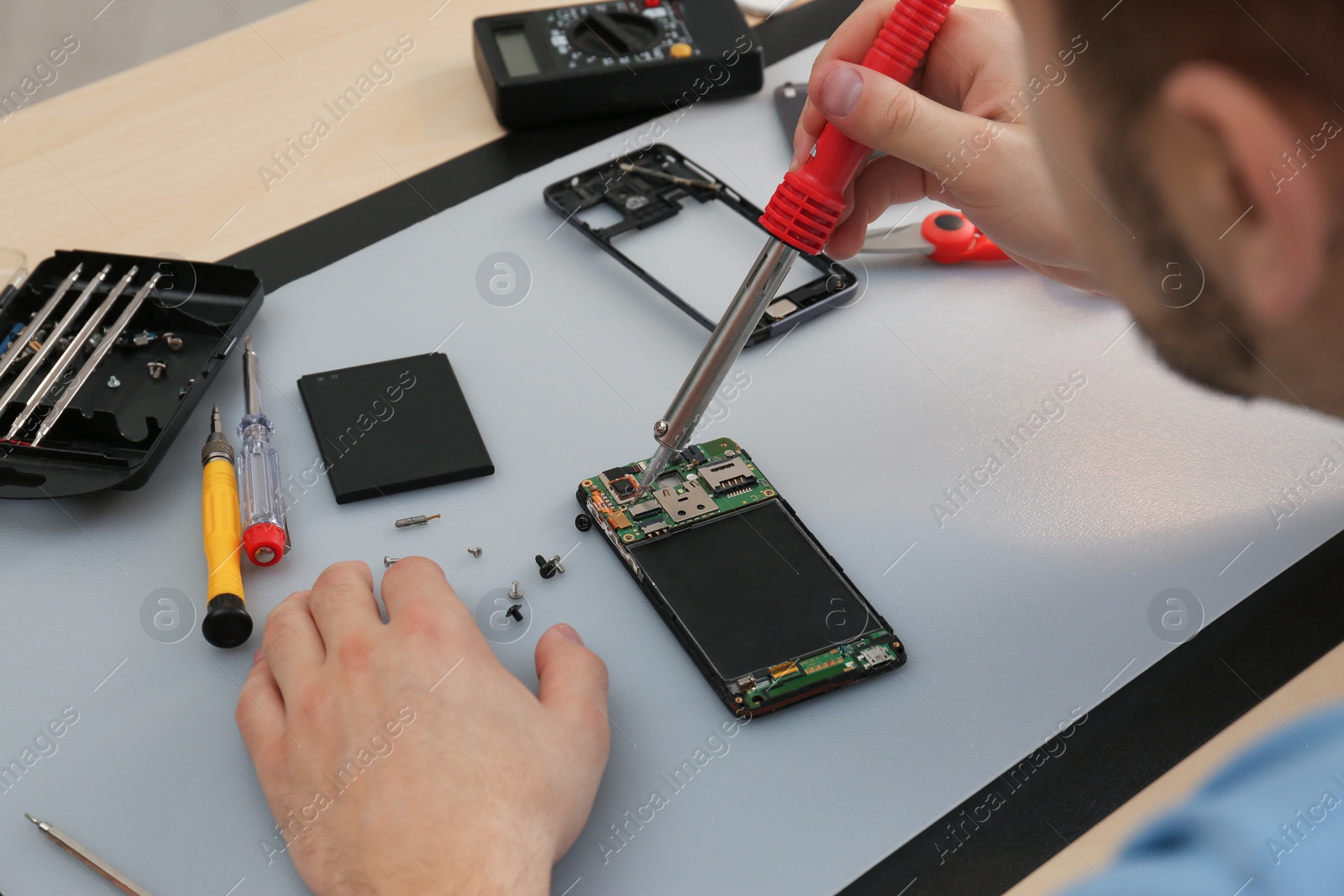 Photo of Technician repairing broken smartphone at table, closeup