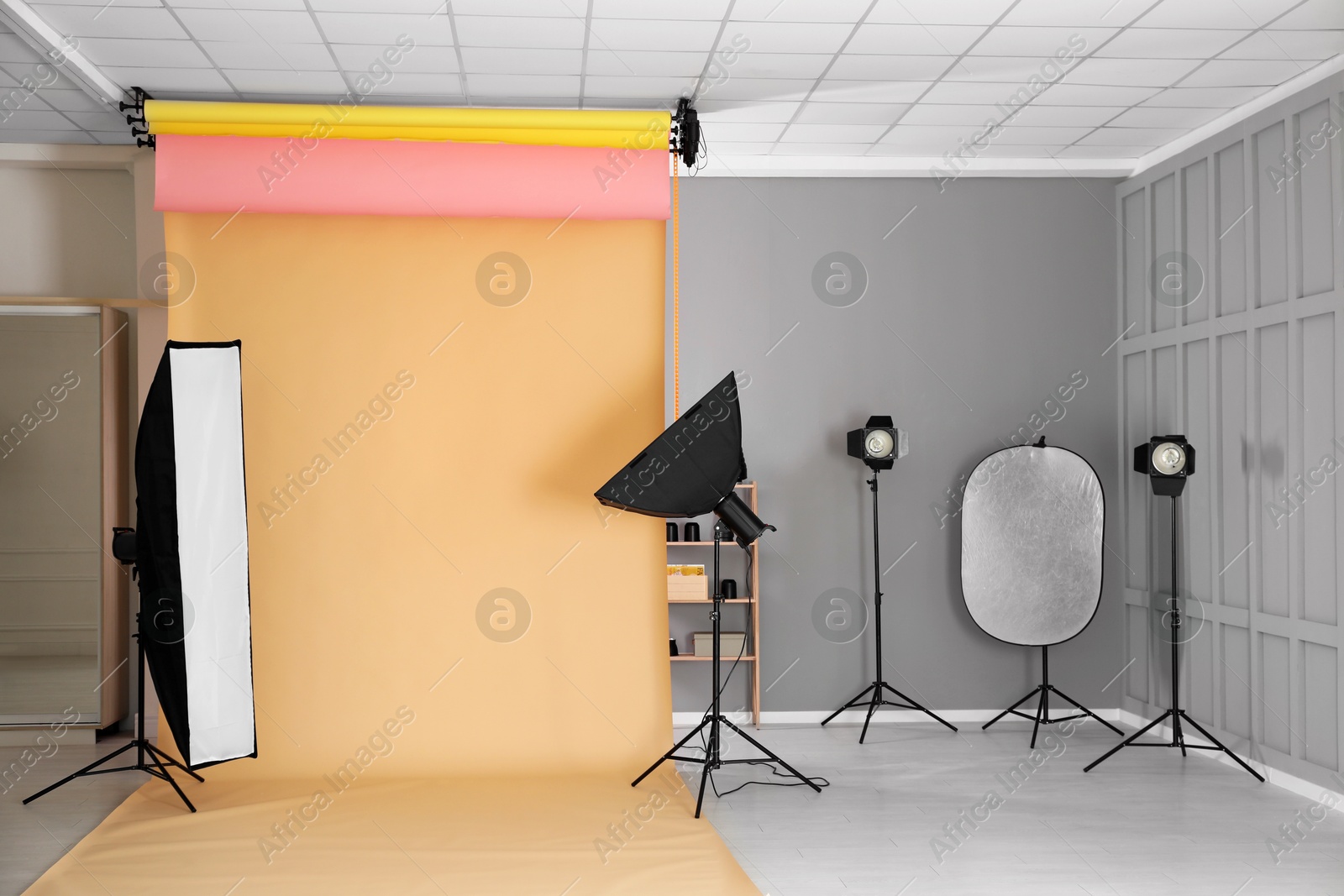 Photo of Pale orange photo background and professional lighting equipment in modern studio