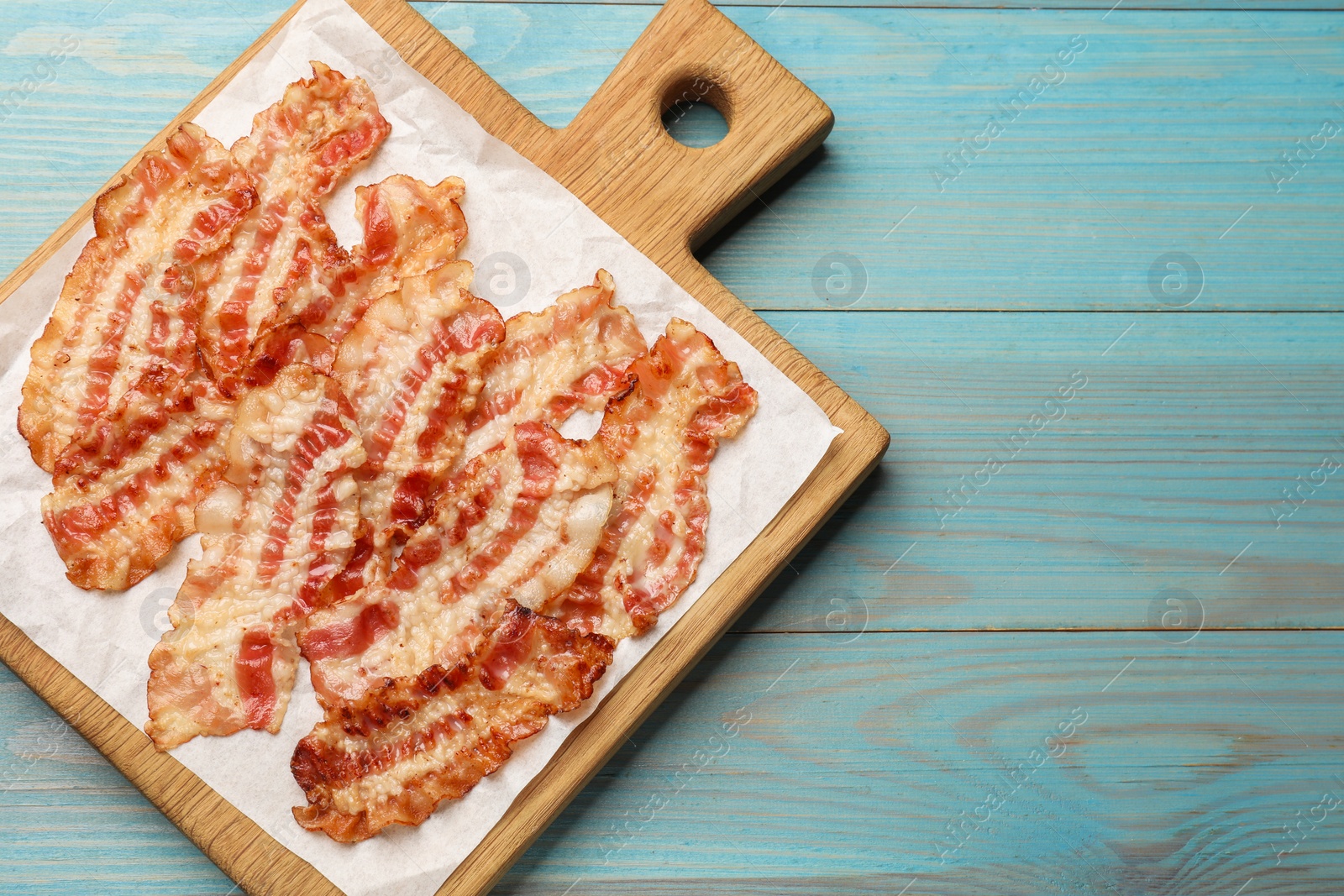Photo of Delicious fried bacon slices on blue wooden table, top view. Space for text