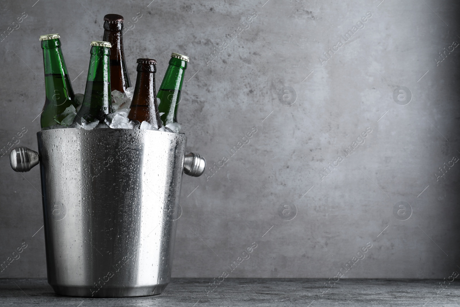 Photo of Metal bucket with bottles of beer and ice cubes on grey table, space for text