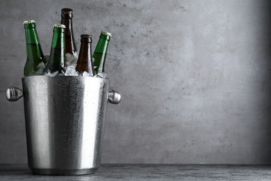 Metal bucket with bottles of beer and ice cubes on grey table, space for text