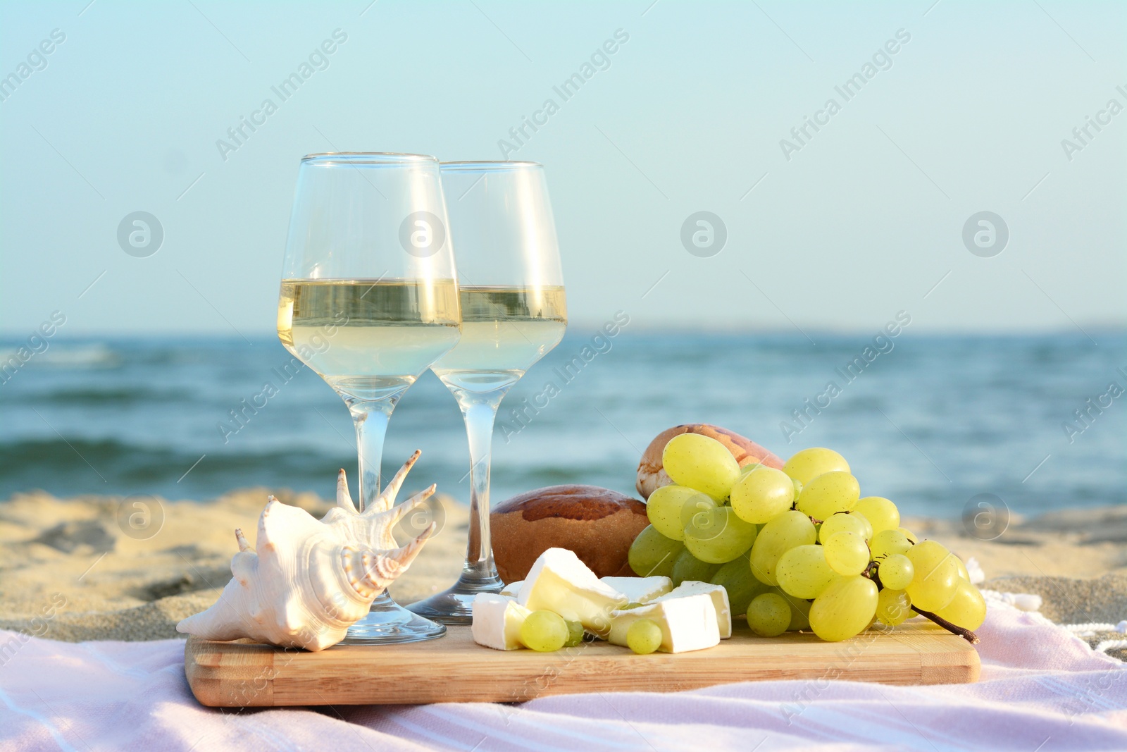 Photo of Glasses with white wine and snacks for beach picnic on sandy seashore