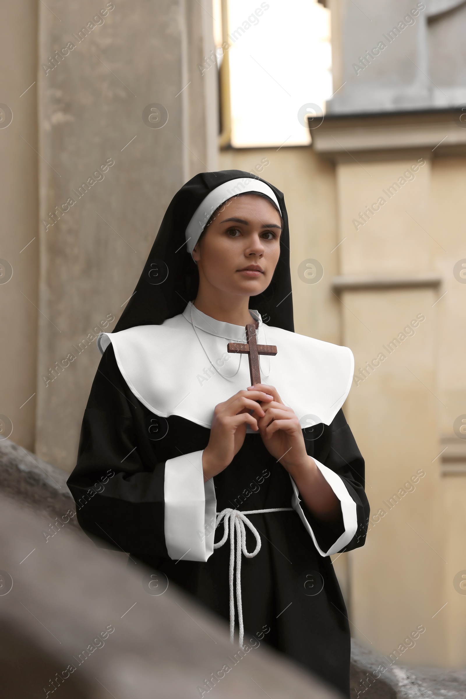 Photo of Young nun with Christian cross near building outdoors