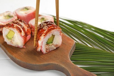 Photo of Taking delicious sushi roll with chopsticks at white wooden table, closeup