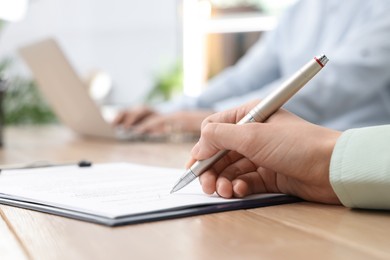 Woman signing contract at table in office, closeup.