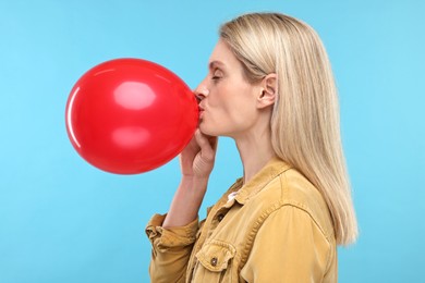 Woman blowing up balloon on light blue background