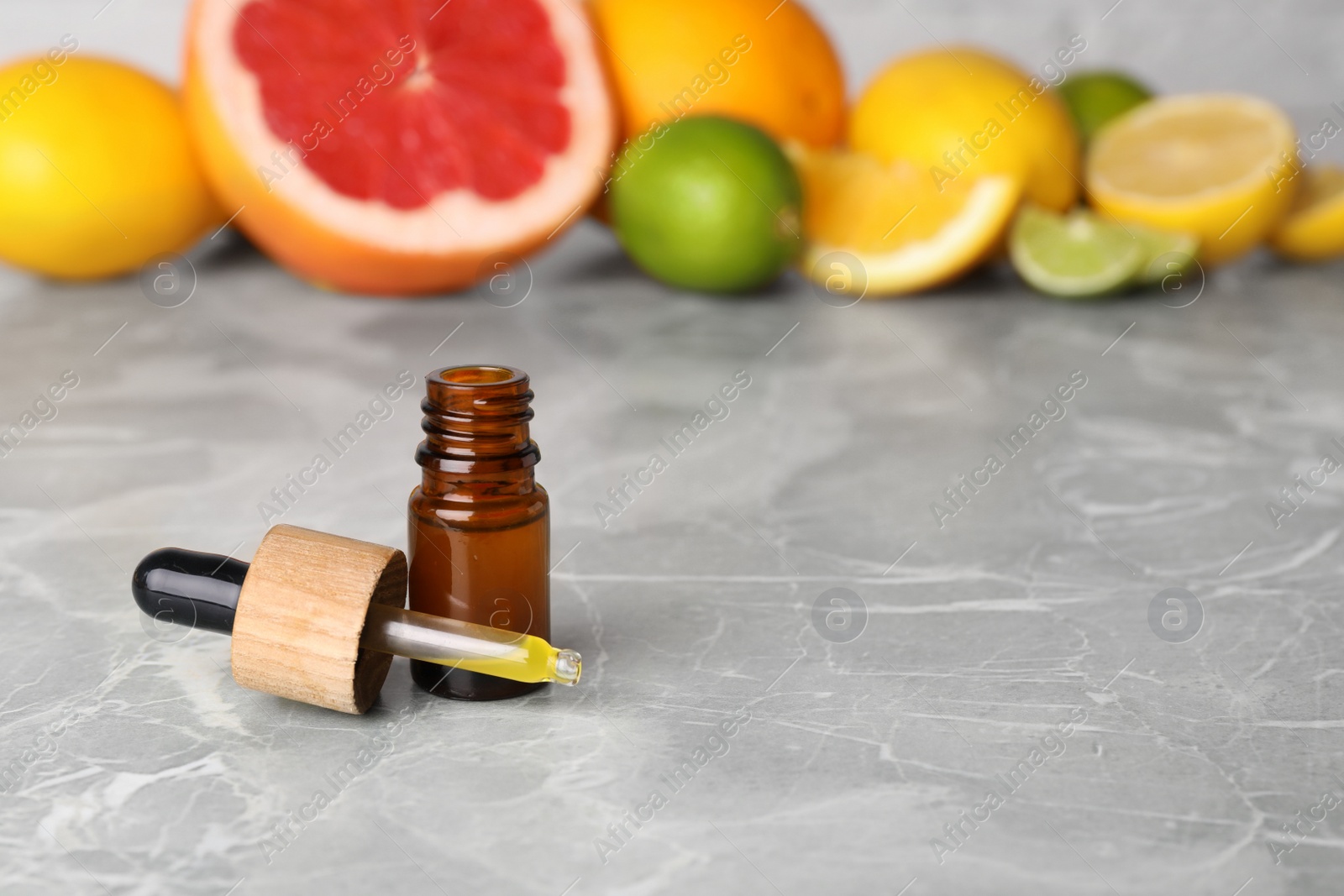 Photo of Bottle of essential oil with different citrus fruits on grey marble table. Space for text